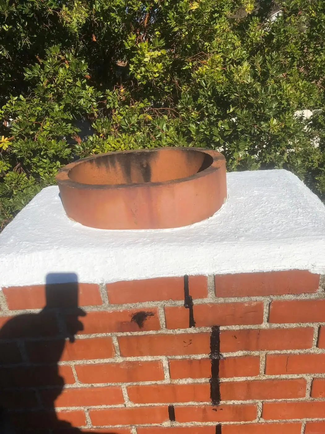 A clay flue tile set in a white crown on a red brick chimney with dark streaks down the brick.