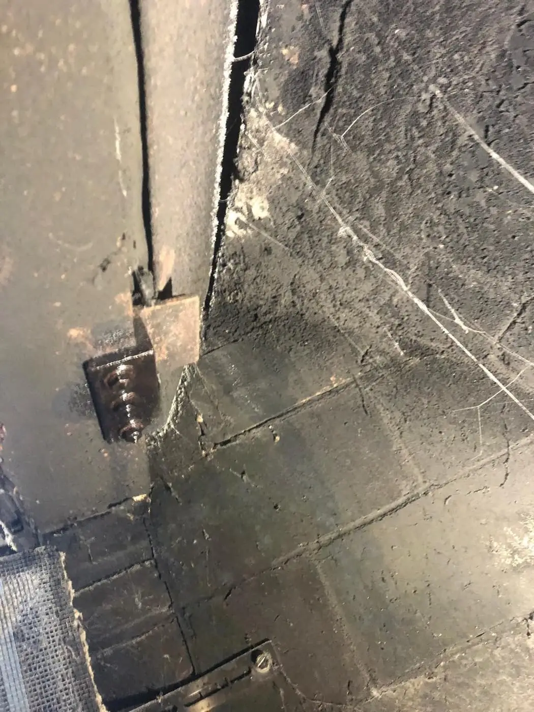 A crack in soot-covered masonry beside a metal frame inside a fireplace.