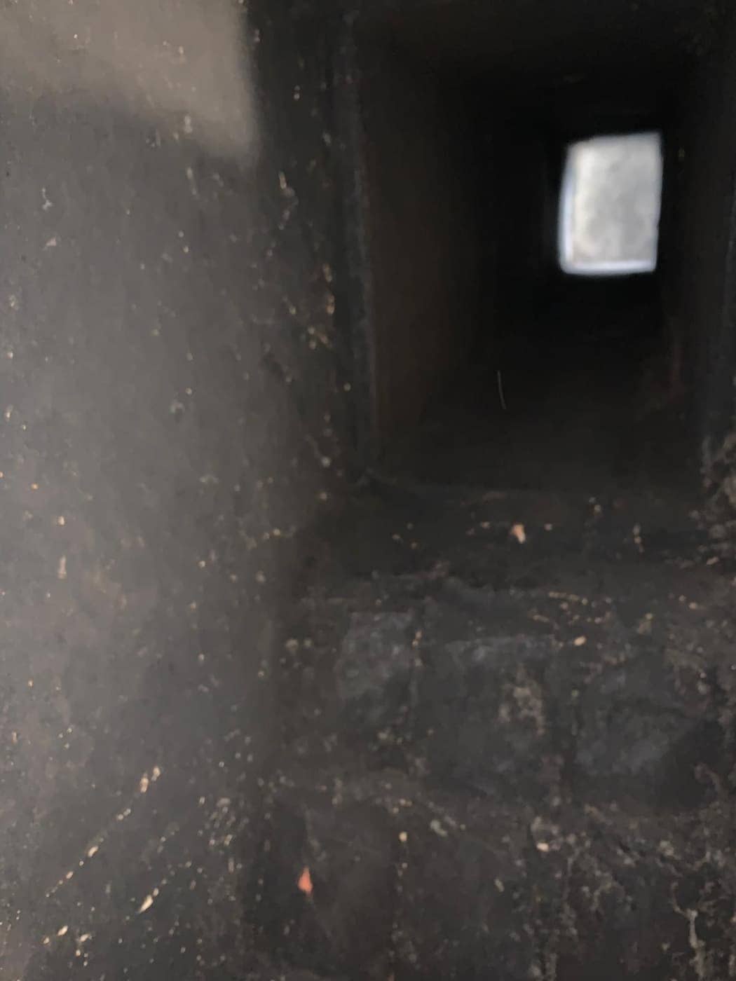 Looking up a dark flue with buildup on its walls toward the opening at the top.