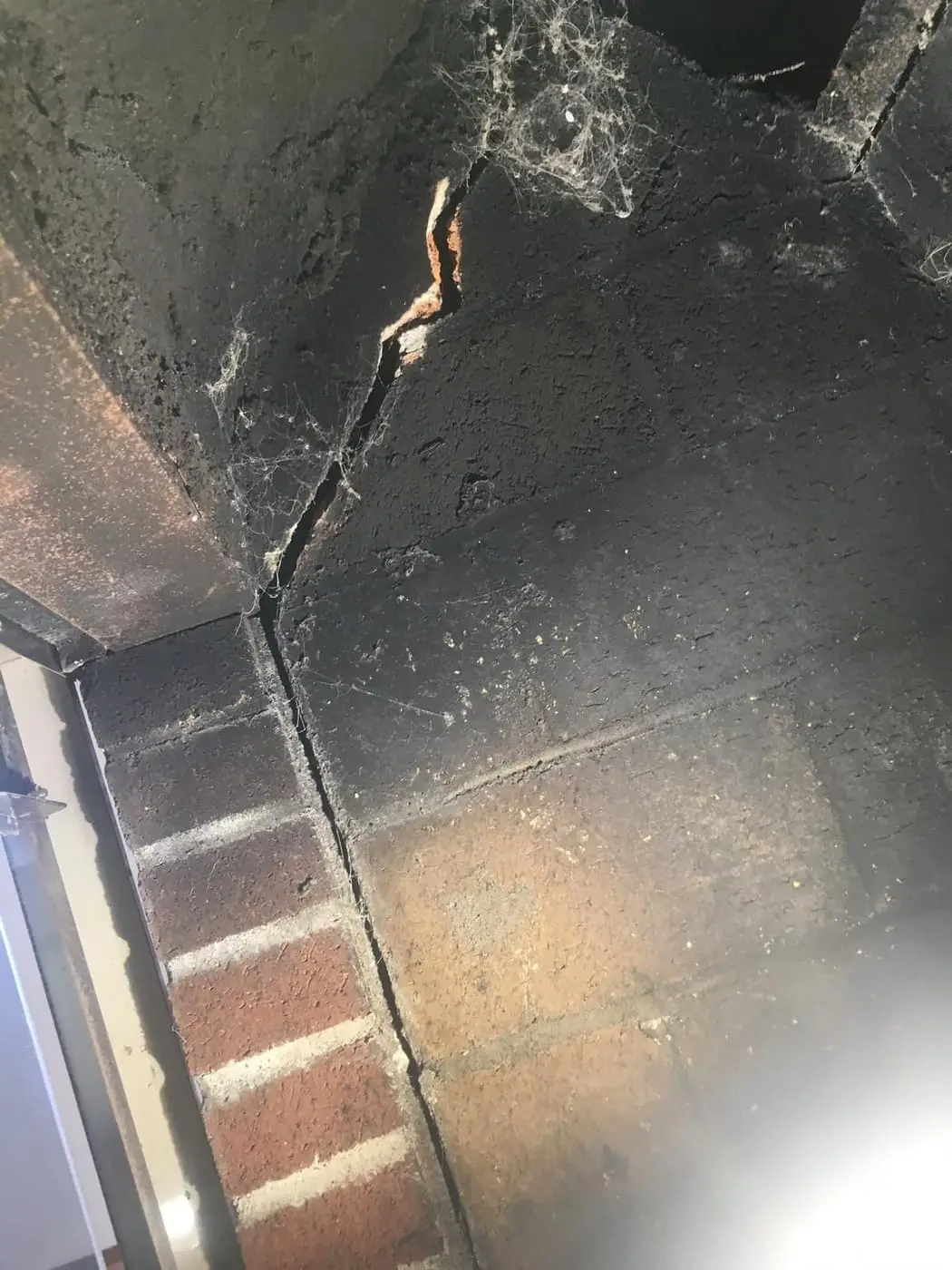 A crack running through soot-darkened masonry inside a fireplace.