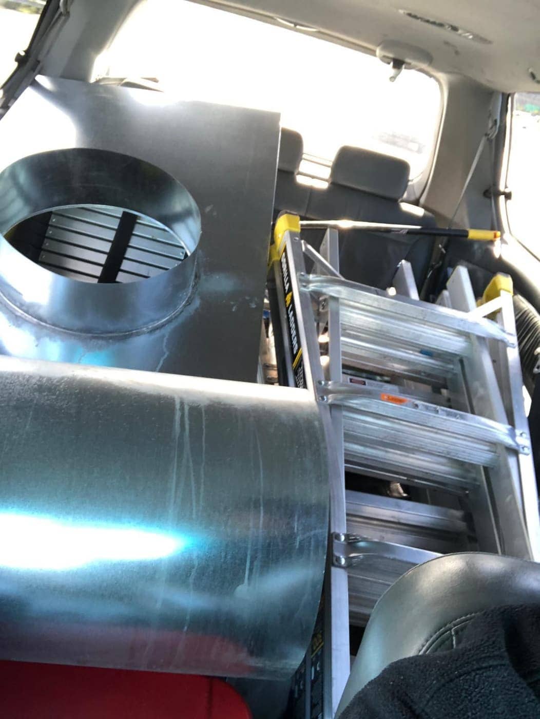 Sheet metal pipe and a round metal fitting loaded in a work vehicle next to a folding ladder.